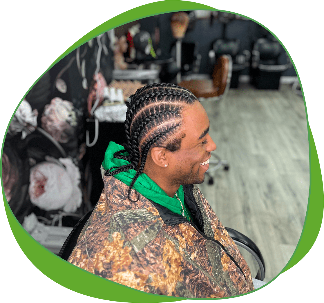 Man with detailed cornrow braids hairstyle sitting indoors.