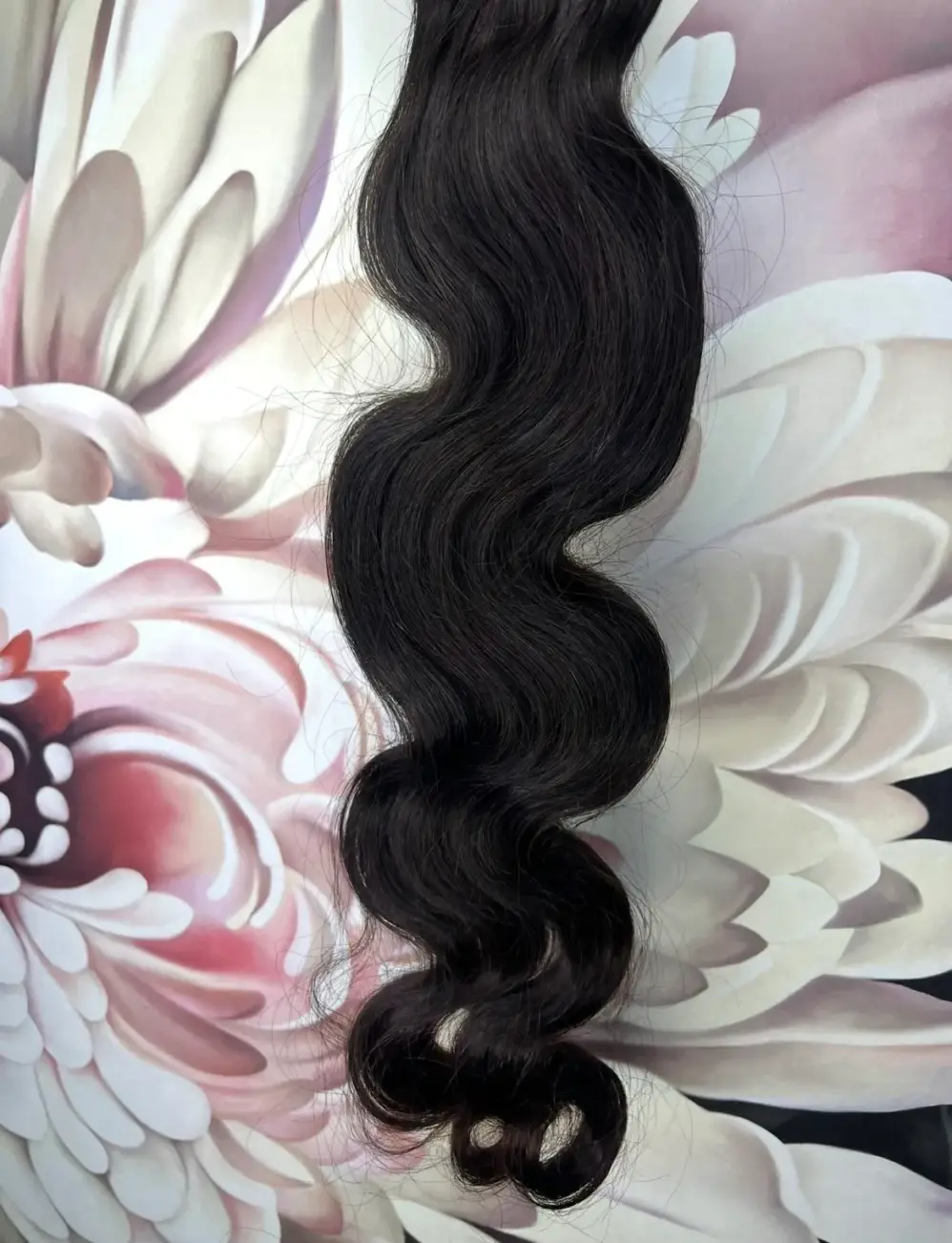 A bundle of dark, wavy hair extension on a floral background.